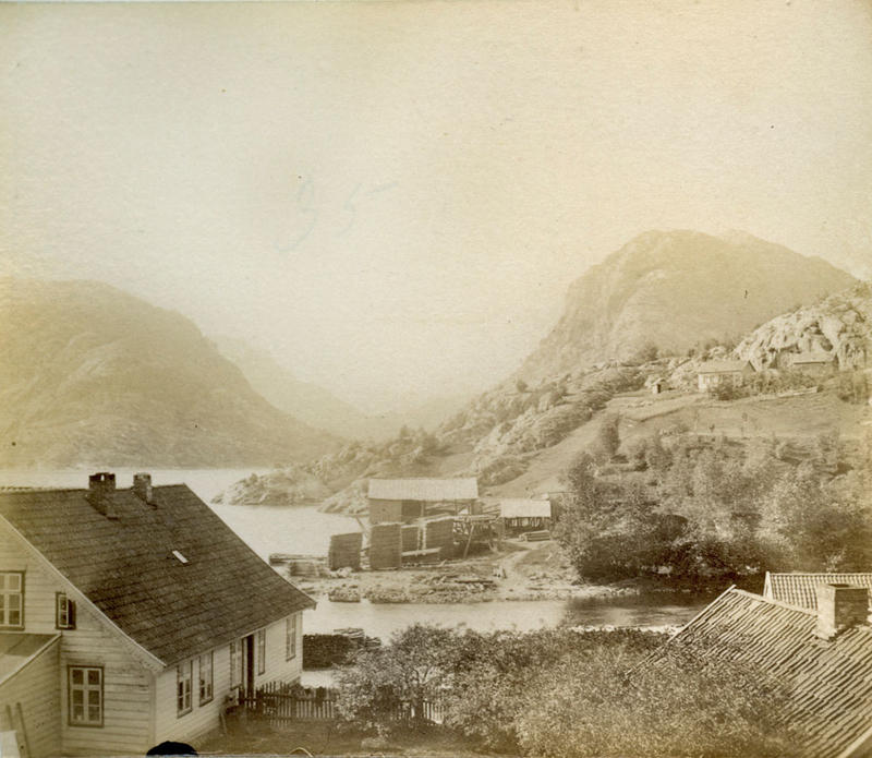  Hålandsosen i Erfjord i 1888. Krambua til venstre dreiv Lars Torjussen Våge frå 1870. I midten på andre sida av elva ser vi Hålandssaga med høge bordstablar på utsida. 