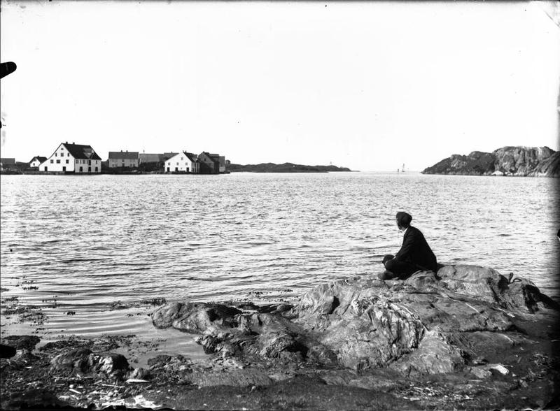 En mann sitter med ryggen til fotografen og skuer utover mot Vibrandsøy, vest for Haugesund. Fotograf: Thea Larsen, MHB-F.003007, Karmsund folkemuseums fotosamling.