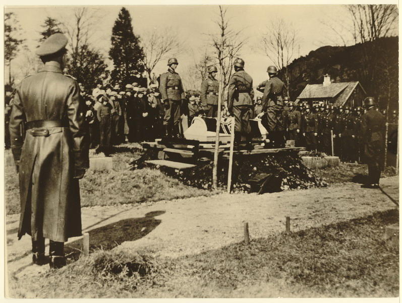Egersund kirkegård, Årstad 17 april 1940. Begravelse av tysk flyger som hadde forulykket. Kisten settes på grava. Ortskomandant Rittmeister Friedrich R. Eickhorn i giv akt. Vi ser at en rekke sivile nordmenn var også møtte fram til gravferden.