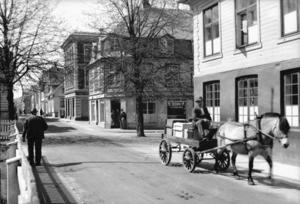 Her er vi i Strandgaten. Baker Haakon Hellvig bringer ut varer med hest og vogn og passerer Middelskolen. Fotografiet er fra ca. 1935.