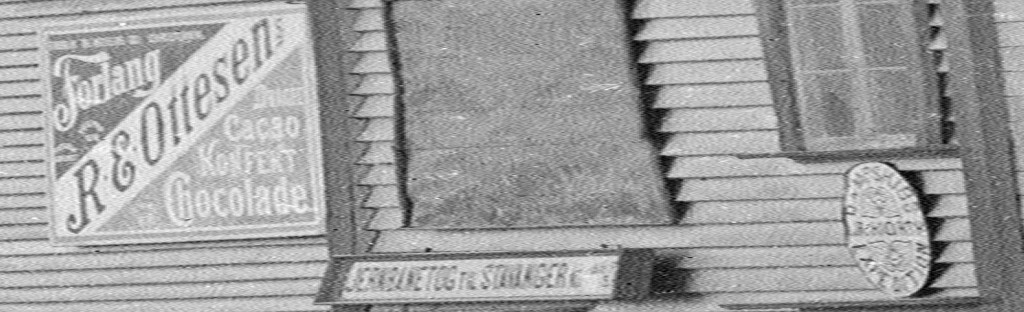 Skilt på dampskipskaien i Egersund. Fra venstre ser vi reklame for "R. E. Ottesens Chokolade", et skilt som forteller om "Jernbanetog til Stavanger" og til slutt logoen til "J. Hiorth Dampskibs Expedition". Ca. 1900. Foto: Erik Hadland Torjusen, DFF-EHT0304 (utsnitt).